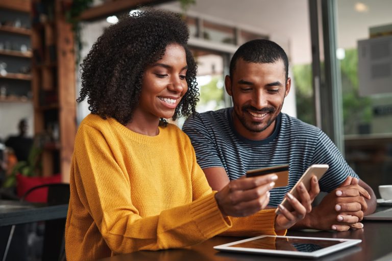 smiling woman entering credit card details on a laptop with her boyfriend watching